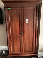 Front view of closed armoire showing double paneled doors, rope twist trim, decorative rosettes and brass knobs.
