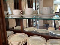 Six cups and saucers on top shelf with stacks of plates below