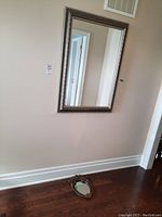 Smaller framed mirror on floor with ornate gold-tone decorative frame showing size contrast with larger mirror