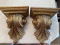 Pair of decorative wall sconces with gold finish, showing details and mounting bases.