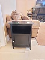 Side view of black wood side table beside a beige couch in a living room.