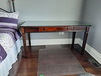 Front view of cherry-colored wood desk with fluted legs and clear glass top fitted over the surface