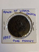 Photo of the obverse side of the 1857 Bank of Upper Canada one penny coin in protective holder with handwritten text.