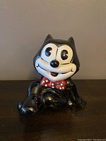Front view of Felix the Cat porcelain piggy bank showing facial details and bow tie, seated pose.