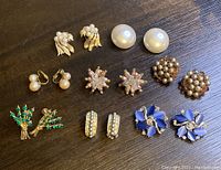 Topview of 8 pairs of vintage clip-on earrings arranged on a wooden surface showing varied designs and colors.