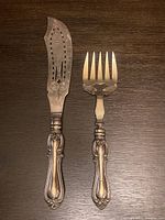 Full view of antique fish serving knife and fork with ornate handles on wooden surface