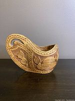 Side profile of the carved wooden Kuska cup showing handle and detailed spiral and geometric carvings.