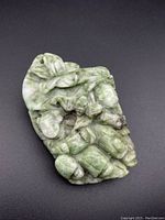 Top view of green carved jade pendant showing detailed figures and carving with natural color variations.