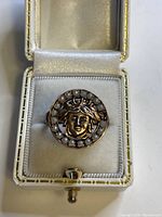 Top-down view of an Italian sterling silver ring with a raised female face and pearl accents on a white cushioned ring box.