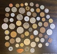 Overview of all coins laid out flat on a dark surface showing the full lot variety including different sizes, colors, and shapes