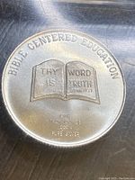 Close-up of the silver round coin with 'Bible Centered Education' inscription and open bible motif.