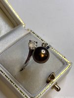 Close-up view of sterling silver ring showing black pearl and clear gemstone on band inside white velvet jewelry box.
