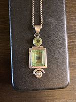Close-up of sterling silver pendant with circular and rectangular green stones on a black background.