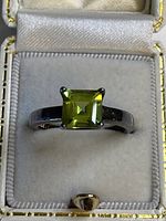 Front view of sterling silver ring with square-cut green gemstone in a white padded ring box.