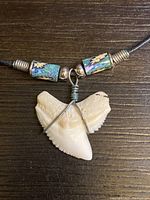 Close-up view of the tiger shark tooth pendant wrapped in wire and decorative blue floral beads on the cord.
