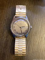 Front view of a vintage Timex automatic wristwatch on an expandable metal band. Day and date visible showing "SAT 12."
