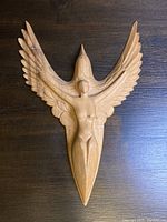 Top view of hand-carved wooden sculpture showing woman merged with bird in flight, highlighting details of wings and human figure.