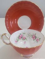 Tea cup front and saucer in background showing floral pattern and coral scalloped saucer edge.