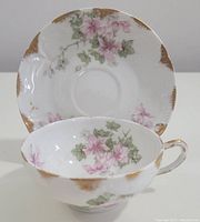 Tea cup positioned inside the saucer showing pink floral patterns and gold rim accents on both pieces.