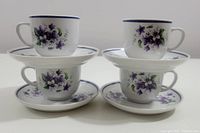 Four Hollohaza demitasse cups and matching saucers stacked in pairs showing the purple floral designs and blue rim.