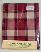 Folded tablecloth packaged in clear plastic with visible plaid pattern in red and cream tones, labeled with brand and fabric information