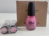 Two Revlon lipsticks labeled #668 Primrose and one Sinful Colors Professional nail polish in pink shade #2195 Jam Out with cardboard box background.