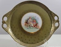 Full view of the oval serving plate showing handles, green background with gold decoration, and the central painted portrait scene.