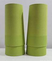 Two green retro style tall lamp shades shown side by side on a white surface against a plain wall.
