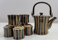 Full set view showing one tea pot and six cups with multi-colored vertical stripes and woven handle on pot