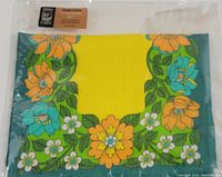 Image of folded placemat showing yellow center with orange, blue, and white floral border and tag