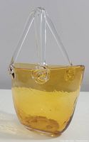 Front and side view of amber blown glass art glass purse with clear glass handles showing shape and color.