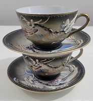Two vintage Betsons hand painted moriage dragonware cups with dragon designs and gold accents stacked atop matching saucers showing detailed artwork and condition.