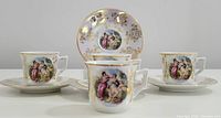 Four vintage demitasse cups and saucers displayed together, showing classical figure artwork and gold floral trim on porcelain.