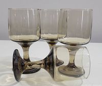 Four smokey brown vintage wine glasses with rounded bowls, short stems, and solid bases shown standing and one laying down to display the shape and color.