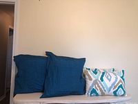 Pair of blue-green square pillows and pair of rectangular pillows with abstract pattern on a white bench