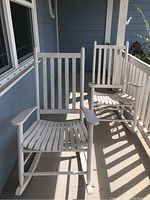 Photo of two white wooden rocking chairs on a porch showing front and side views, slatted seat and back, and rockers.