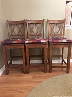 Front view of three medium wood island bar chairs with cushions on seats.