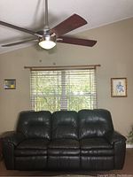 Front view of dark brown vinyl reclining sofa placed in living room with ceiling fan and wall decor.