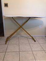 Full view of yellow metal ironing board standing upright with white cover, showing X-shaped legs and rubber feet.