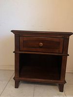 Front view of the nightstand showing drawer, open lower shelf, and decorative details.