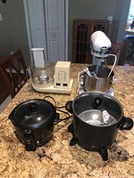 Photo showing four kitchen appliances: Hamilton Beach food processor, KitchenAid stand mixer with bowl and attachments, Presto multi cooker, and Chef's Counter rice cooker, all on a granite surface.