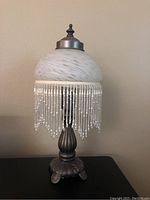 Front view of small decorative lamp with marbled glass shade and clear beaded fringe, on bronze-tone ornate base.