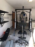 Wide view showing weight station with dumbbells laid out in front, additional workout bench visible beside the station.