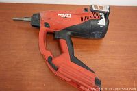 Photo of the full Hilti GX 120 tool showing the red and black body, pistol grip handle, and metal nose piece.
