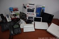 Wide angle view of the lot showing phones, tablets, keyboards, headphones and boxed electronic accessories on a wooden surface.