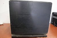 Front and side view of black wood-finished rectangular subwoofer cabinet with visible surface wear.