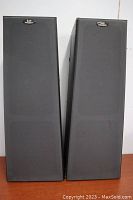 Pair of floor-standing speakers with black speaker grills on, showing profiles and overall front view.