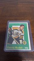 Front image of the 1959-60 Topps Fleming Mackell hockey card in a protective plastic case showing player wearing Boston Bruins jersey with green background.