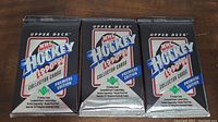 Three sealed 1990-91 Upper Deck NHL Hockey Hockey Collector Card packs stacked side by side on a wooden surface.