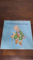Front cover of April Wine vinyl album 'The Whole World's Goin' Crazy' with cartoon artwork on light blue background.